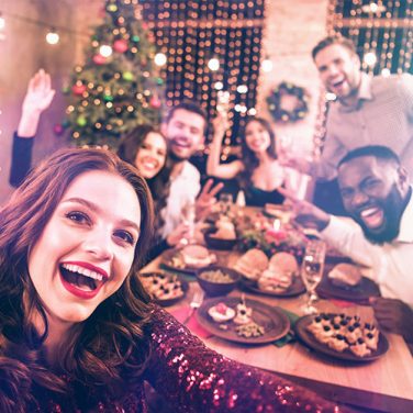 Group selfie in front of a Christmas dinner table with Christmas tree and fairy lights in the background.