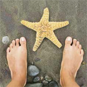Looking down at a bare feet on the beach and a star fish.
