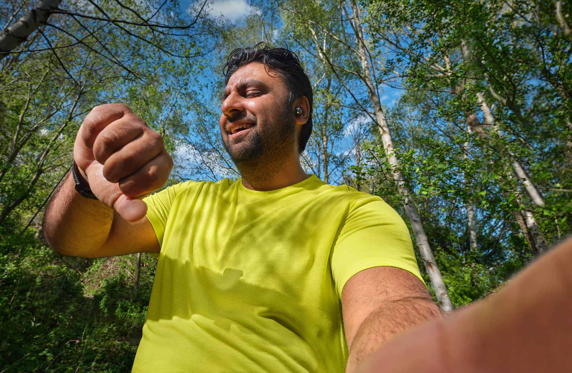 Photo of a man in a wooded area looking at his watch.