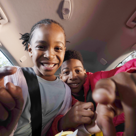 Image of two smiling children inside car pointing at the camera.