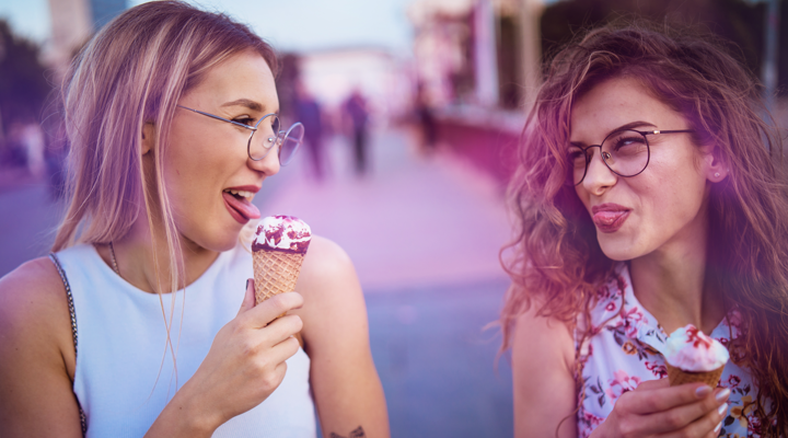 Two girls eating ice creams and sticking their tongues out at each other playfully