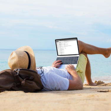 Man laying back and checking his email on his laptop on the beach
